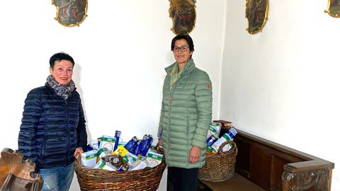  Zwei Frauen mit Körben voller Lebensmittel in einer Kirche. Rosl Baur und Susanne Backes-Keck kümmern sich ehrenamtlich um die Körbe mit Lebensmitteln, die in katholischen Kirchen in Niederstotzingen für Bedürftige bereitstehen. (Foto: SWR, Maja Nötzel)