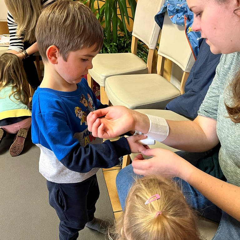 Erste-Hilfe-Kurs für Kinder in Schwäbisch Gmünd (Ostalbkreis): Ein kleiner Junge übt am Arm seiner Mutter, wie man einen Verband anlegt.