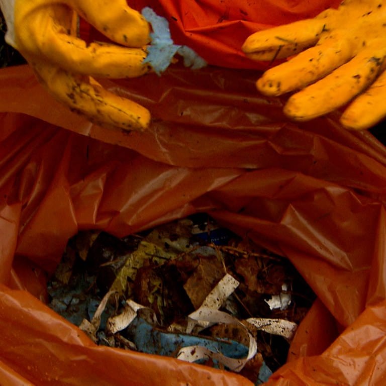 Ein Helfer zeigt einen Müllsack mit kleinen Teilen von Plastikverpackungen.