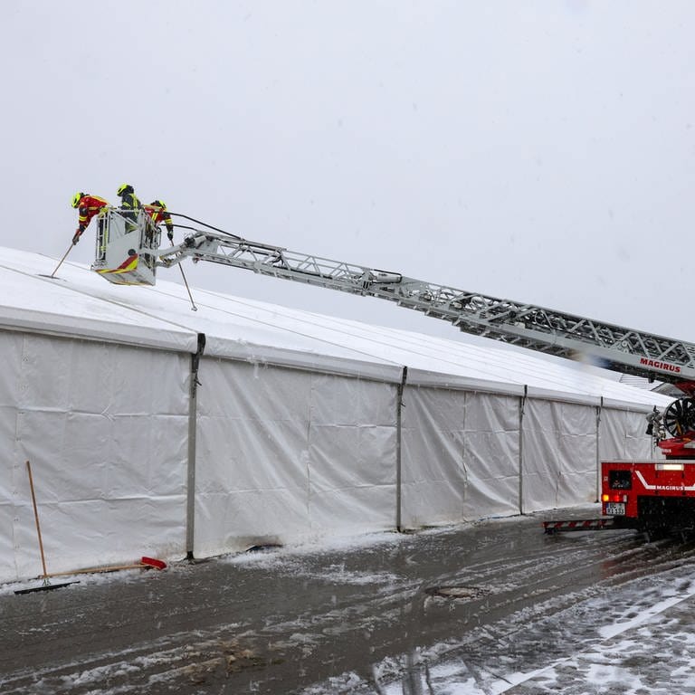 Feuerwehrleute stehen im Korb einer Drehleiter über dem Dach des Festzeltes in Riedlingen-Zell (Kreis Biberach).  Sie kehren Schnee vom Zelt.  (Foto: Thomas Warnack)
