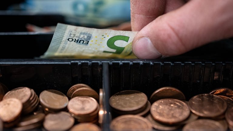 Hand nimmt 5-Euro-Schein aus Kasse