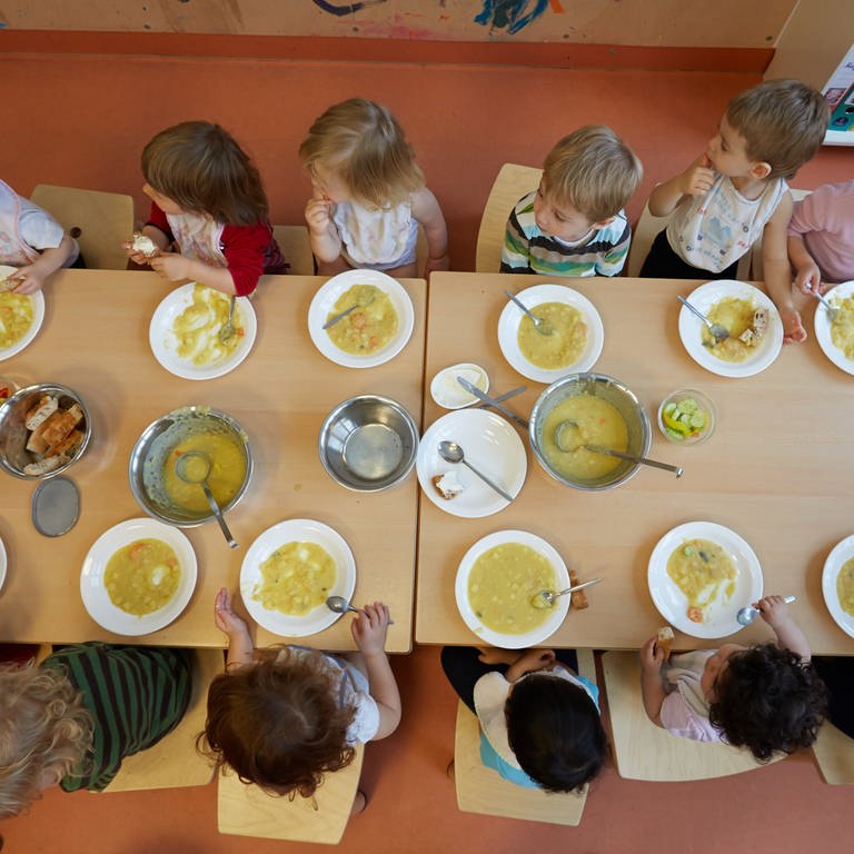 Kinder in einer Kita sitzen gemeinsam an einem Tisch beim Mittagessen.