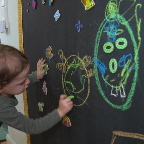 Kind malt mit bunter Kreide auf eine Tafel