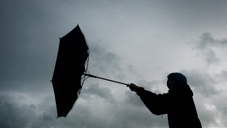 Frau hält im Sturm einen Regenschrim.