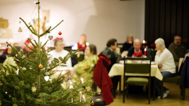 Menschen sitzen gemeinsam an Weihnachten zusammen und feiern. Vereine und Organisationen in Koblenz und der Region organisieren kleine Weihnachtsfeiern für alleinstehende Menschen, die an Heiligabend sonst allein wären.