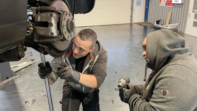 Zwei Männer schrauben an einem Auto. Manuel Saba betreibt in Gau-Algesheim eine Hobby-Werkstatt, wo Menschen ihr Auto selbst reparieren können. (Foto: SWR, Alexander Dietz)