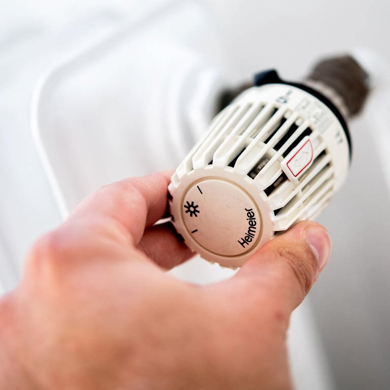 Ein Mann dreht in einer Wohnung am Thermostat einer Heizung. Die Wohnbau Mainz will die Temperaturen im Winter verringern, um Energie zu sparen.