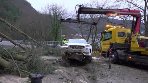 Ein Auto wird nach dem Hangrutsch mit mehreren umgestürzten Bäumen von der B53 weggeräumt. Es war in der Nacht zum Sonntag mit dem Bäumen kollidiert. (Foto: Winkler TV)