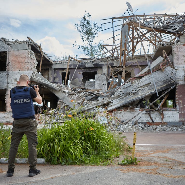 Ein Fotoreporter mit der Veste "Press" fotografiert bombardierte Gebäude