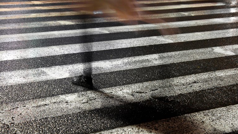 Pedestrian on rainy city street, Rainy city street reflections: One young fragile female disappearing while crossing the wet street in the sparkling night (Foto: IMAGO, Dreamstime)