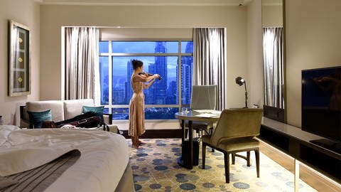 Eine Frau spielt Geige in einem modernen Hotelzimmer. 