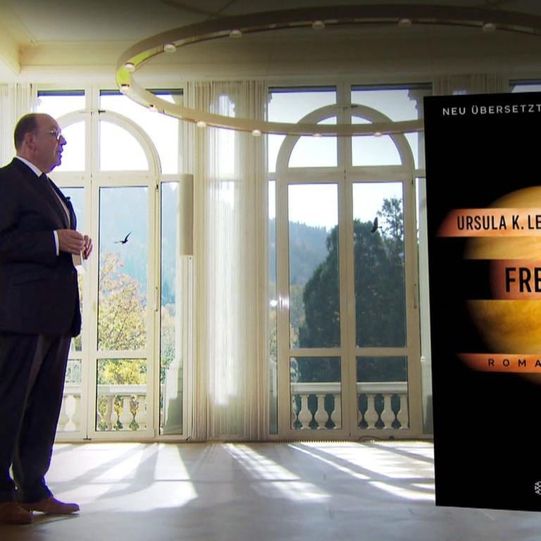 Denis Scheck steht neben dem Buch "Freie Geister" von Ursula K. Le Guin