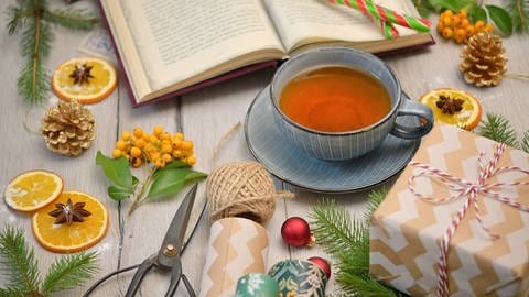 Ein Buch, Geschenkpapier und eine Tasse Tee mit winterlicher Dekoration