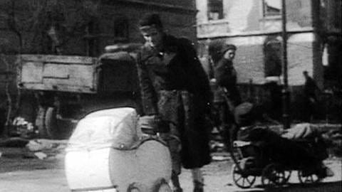 Frau schiebt in Trümmern einer Stadt nach dem 2. Weltkrieg einen Kinderwagen