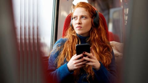 Eine Frau mit Kopfhörern während einer Bahnfahrt  (Foto: IMAGO, imago images/Image Source)