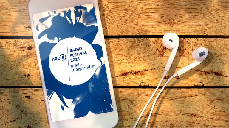 Ein Smartphone mit dem Logo des ARD Radiofestivals 2023 und Ohrstöpseln liegt auf einer Holzpaneele