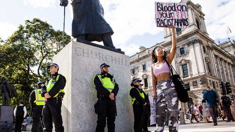 Bei den #BlackLivesMatter- und Anti-Rassismus-Demonstrationen in London hält am 20. Juni 2020 eine Frau ein Plakat mit der Aufschrift "Blood on your racist hands" in die Höhe. Polizisten bewachen die Statue von Winston Churchill.