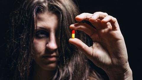Junge Frau hält eine Pille in ihren Fingern und betrachtet diese.