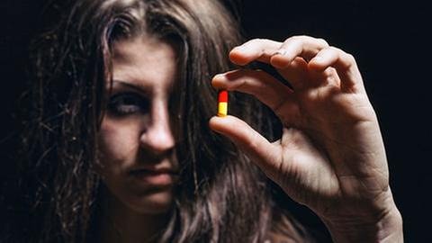 Junge Frau hält eine Pille in ihren Fingern und betrachtet diese. (Foto: Colourbox, Model Foto: Colourbox.de -) Junge Frau hält eine Pille in ihren Fingern und betrachtet diese.