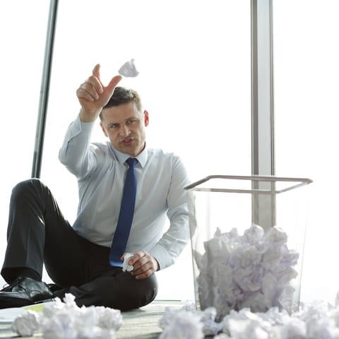 Geschäftsmann sitzt auf der Büroetage, umgeben von zerknittertem Papier (Foto: IMAGO, IMAGO / Westend61)