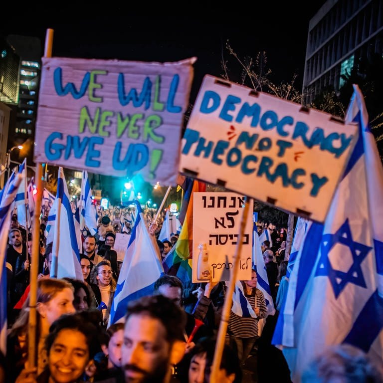 Demonstranten halten am 25. März 2023 in Tel Aviv  Israel Fahnen und Plakate in die Höhe. Auf einem steht "Democracy not Theocracy". Der Protest richtet sich gegen Pläne der Regierung, das Justizsystem umzustrukturieren.  (Foto: picture-alliance / Reportdienste, picture alliance / ZUMAPRESS.com | Eyal Warshavsky)