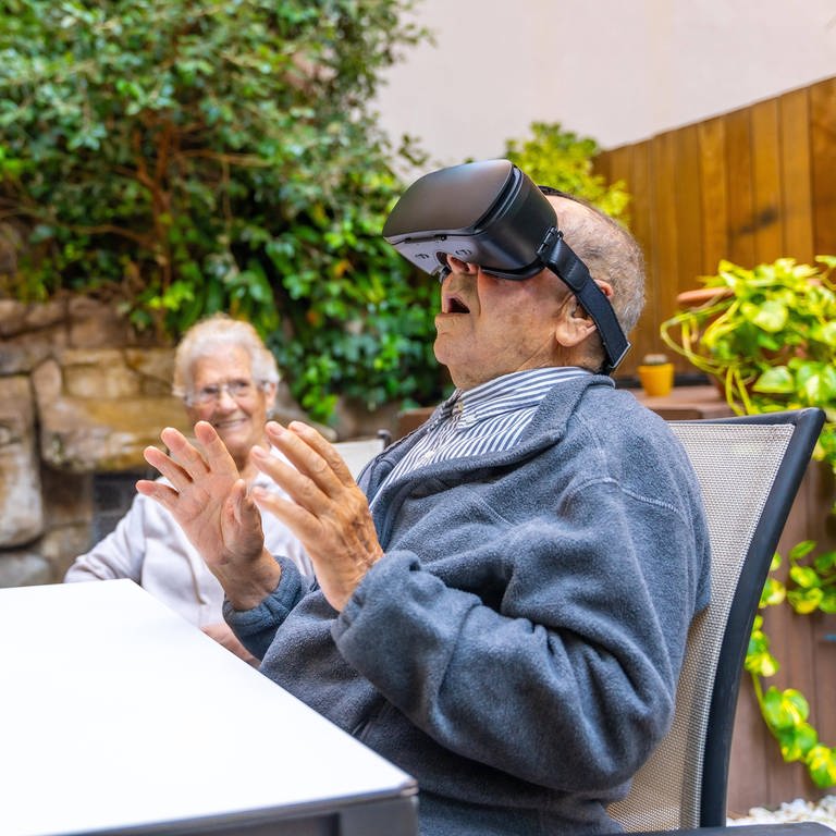 Älterer Mann mit Virtual Reality Brille im Garten eines Pflegeheims.