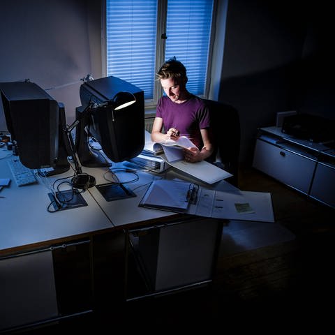 Gestellte Aufnahme zum Thema ' Überlastung am Arbeitsplatz '. Ein Mann arbeitet nachts in einem Buero an einem Computer.