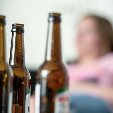 Eine junge Frau sitzt hinter leeren Bierflaschen. (zu dpa "Mehr Hilfen für Kinder von suchtkranken Eltern gefordert")