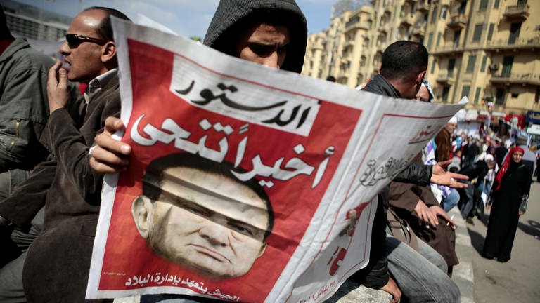 Husni Mubarak ist zurückgetreten; ein Mann liest die Meldung in der Zeitung. Menschen feiern am 12. Februar auf dem Tahrir-Platz in Kairo  Ägypten