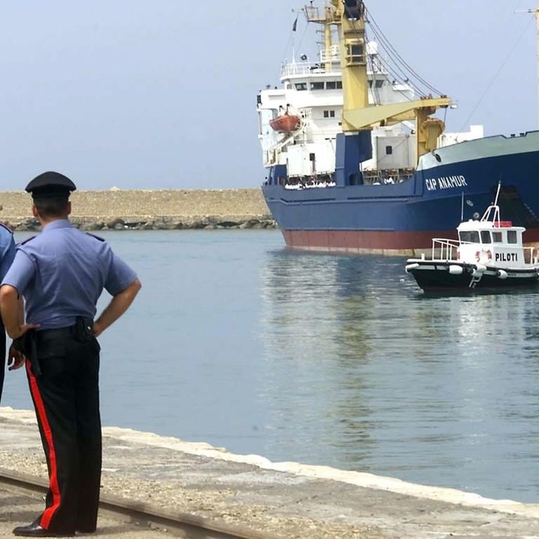 Italienische Polizisten schauen am 12. Juli 2004 auf das deutsche Rettungsschiff "Cap Anamur" beim Anlegen im sizilianischen Hafen Porto Empedocle (Foto: picture-alliance / Reportdienste, picture alliance / ASSOCIATED PRESS | Alessandro Fucarini)
