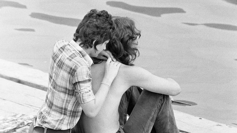 Junges Paar sitz an einem Ufer, Anfang 1970er-Jahre