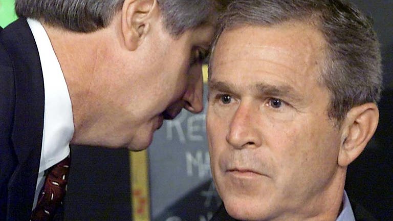 George W. Bush erfährt beim Besuch der Grundschule in SarasotaFlorida von den Anschlägen auf das World Trade Center in New York: Sein Stabschef Andy Card flüster dem Präsidenten ins Ohr: "America is under attack" – "Amerika wird angegriffen"