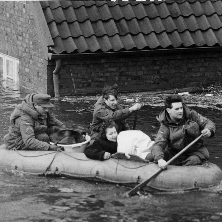 Eine Frau wird während der Sturmflut am 17. Februar 1962 mit einem Schlauchboot in Sicherheit gebracht. Das Wasser reicht fast bis zum Dach des Backsteinhauses im Hintergrund