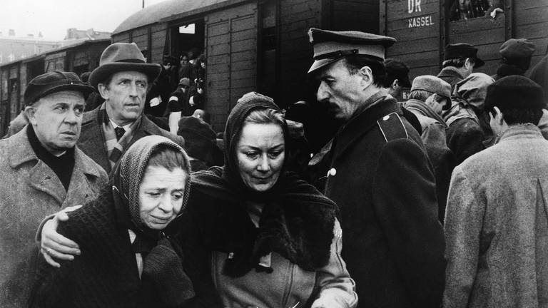 Filmszene Fernsehserie "Holocaust": Zwei Frauen in einer Menschenmenge halten sich im Arm, im Hintergrund ein Güterzug mit Menschen gefüllt
