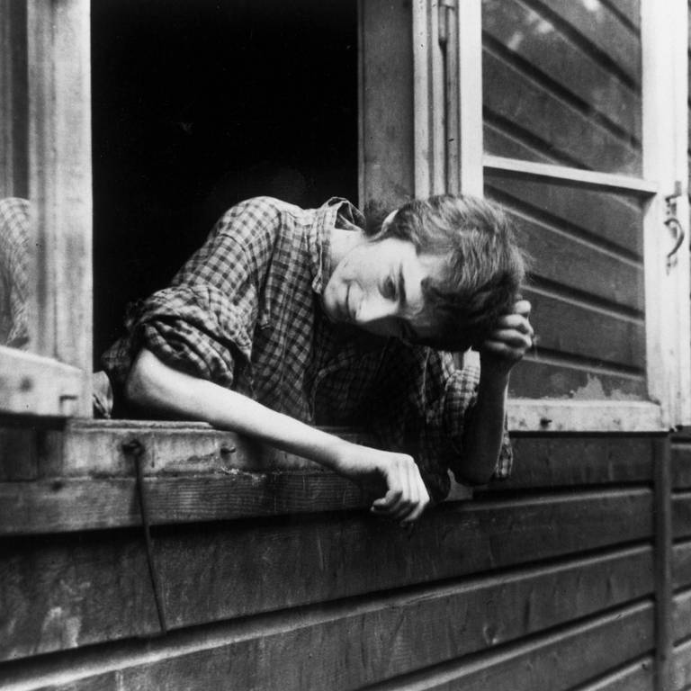 Überlebende Frau schaut in Bergen-Belsen aus dem Fenster einer Baracke, nachdem das Konzentrationslager am 15. April 1945 durch britische Truppen befreit worden war. Die Soldaten fanden Tausende unbestattete Leichen und Zehntausende todkranke Menschen vor, die an Typhus, Ruhr und anderen Krankheiten litten.