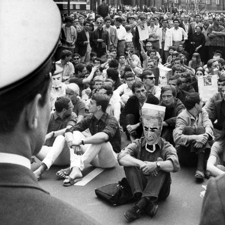 Demonstranten im Sitzstreik werden am 2.6.1967 vor dem Rathaus Schöneberg in Berlin von der Polizei beobachtet. Die Demonstranten protestierten gegen den Besuch des persischen Herrschers Schah Reza Pahlevi. Bei den Zusammenstößen zwischen Demonstranten und Polizei die später am Tag folgten wurde der Student Benno Ohnesorg erschossen.