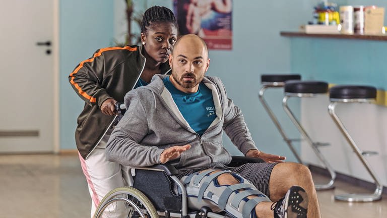 Sidney (Precious Wiesner) schiebt Finn (Bozidar Kocevski), der mit gebrochenem Bein im Rollstuhl sitzt