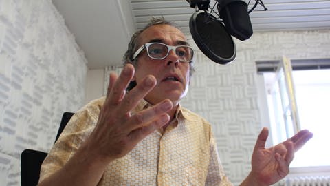 Das Bild zeigt Harald Holz, wie er in ein Mikrofon spricht