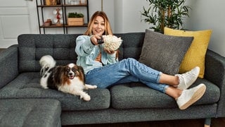 Frau sitzt mit Hund auf der Couch und sieht fern