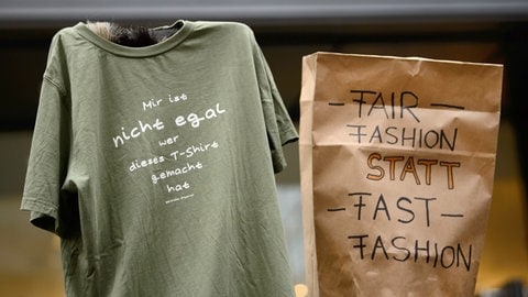Demonstranten halten in Stuttgart ein T-Shirt mit der Aufschrift "Mir ist nicht egal wer dieses T-Shirt gemacht hat" und eine Tüte mit der Aufschrift "Fair Fashion statt Fast Fashion" hoch. (Foto: dpa Bildfunk, picture alliance/Sina Schuldt/dpa) Demonstranten halten in Stuttgart ein T-Shirt mit der Aufschrift "Mir ist nicht egal wer dieses T-Shirt gemacht hat" und eine Tüte mit der Aufschrift "Fair Fashion statt Fast Fashion" hoch.