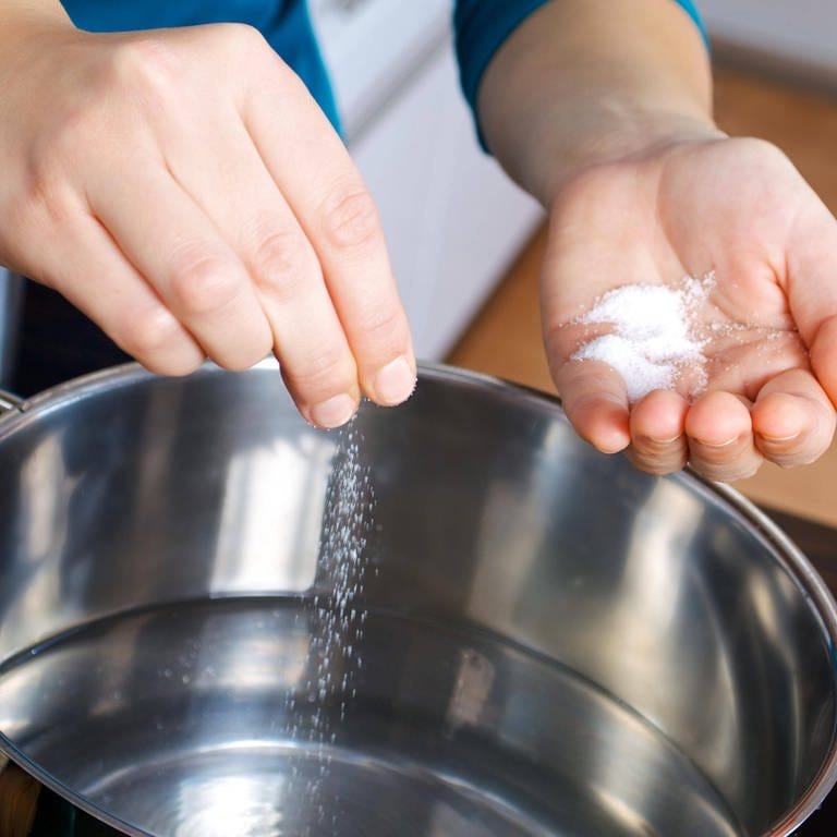 Eine Frau gibt Salz in einen Topf mit Wasser: Kocht gesalzenes Wasser schneller?