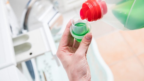 Flüssiges Waschmittel wird eingefüllt: Tenside, Enzyme, Bleichmittel und Mizellen helfen, die Wäsche sauber zu bekommen. Wie genau funktioniert das? Und was hilft gegen welche Flecken? (Foto: picture-alliance / Reportdienste, picture alliance / dpa-tmn | Christin Klose)
