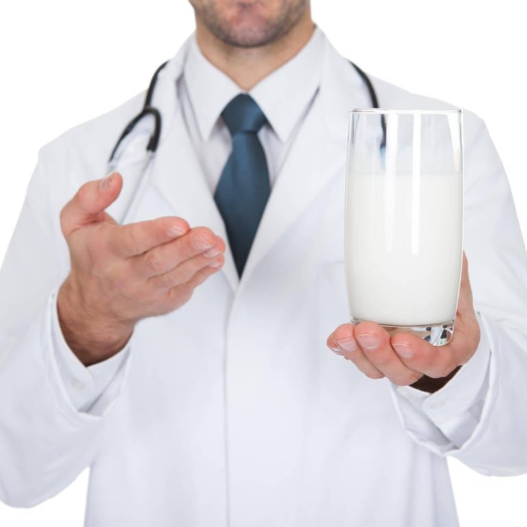 Arzt zeigt auf ein Glas Milch: Stimmt es, dass man Antibiotika nicht mit Milch einnehmen sollte? (Foto: IMAGO, IMAGO / Panthermedia)