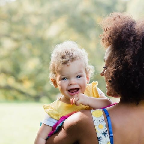 Baby lacht über die Schulter eines Erwachsenen in Richtung Kamera (Foto: IMAGO, IMAGO / Westend61)