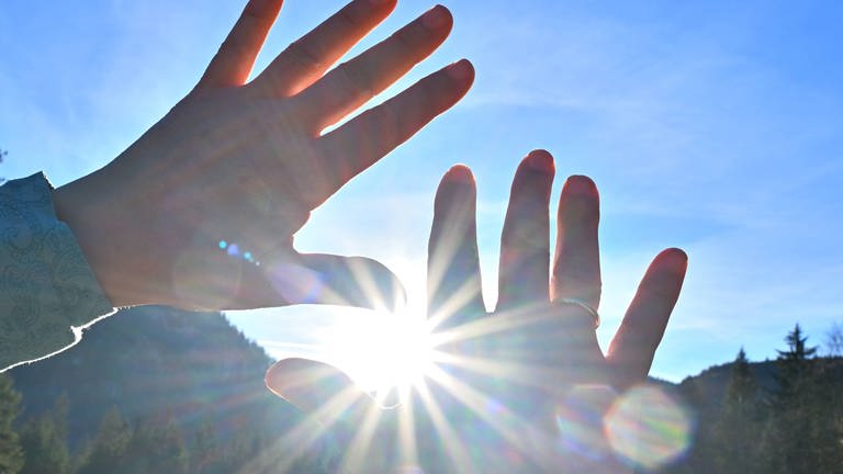 Hände werden versucht schützend vor Sonnenstrahlen zu halten, aber die Sonnenstrahlen kommen zwischen den Fingern durch. (Foto: IMAGO, IMAGO / Rolf Poss)