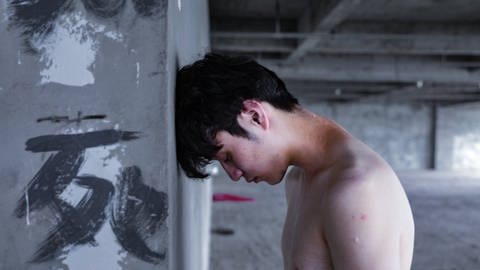 Junger Mann mit Kopf gegen Wand gelehnt: Junge Männer begeben sich bisher seltener in Behandlung und verstecken ihr selbstverletzendes Verhalten, oder sind aggressiv gegen andere Personen als sich selbst (Foto: IMAGO, IMAGO / Imaginechina-Tuchong) Junger Mann mit Kopf gegen Wand gelehnt: Junge Männer begeben sich bisher seltener in Behandlung und verstecken ihr selbstverletzendes Verhalten, oder sind aggressiv gegen andere Personen als sich selbst