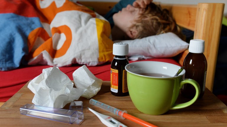 Ein Junge liegt mit Fieber im Bett. Vor ihm auf dem Tisch steht ein Fiebersaft (Foto: picture-alliance / Reportdienste, / Frank May)