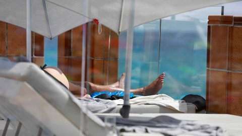 Ein Mann sonnt sich auf einer Hotelterrasse bei starker Sonne. (Foto: IMAGO, picture alliance/dpa | Clara Margais) Ein Mann sonnt sich auf einer Hotelterrasse bei starker Sonne.