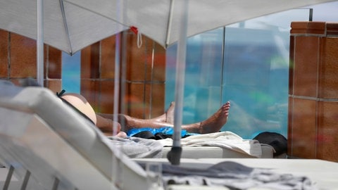 Ein Mann sonnt sich auf einer Hotelterrasse bei starker Sonne. (Foto: IMAGO, picture alliance/dpa | Clara Margais)