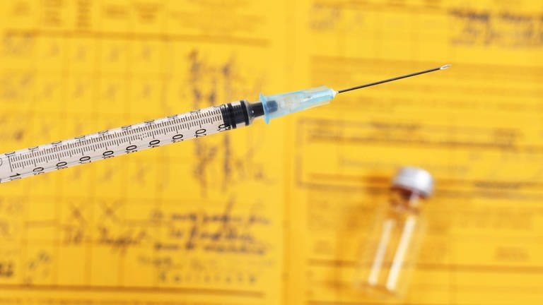 Das Bild zeigt eine Impfspritze mit Impfpass im Hintergrund.